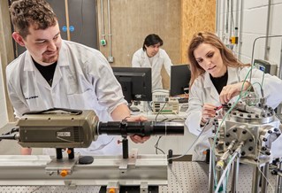 Three researchers wearing white lab coats, working with machinery and digital screens in the ϲʹ Advanced Engineering Centre